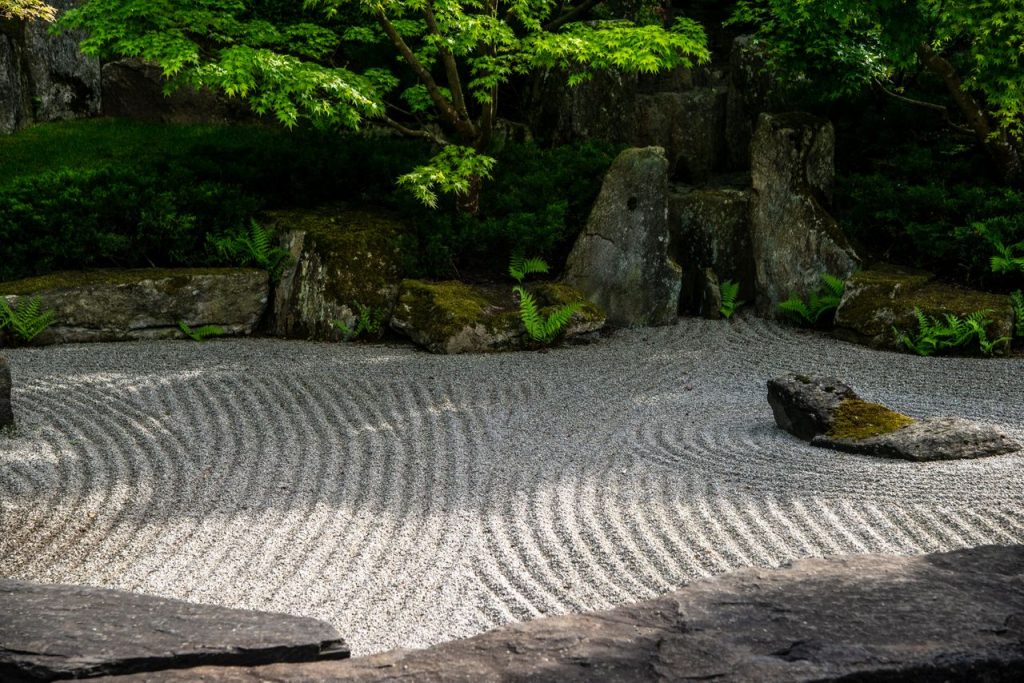 Peaceful Japanese Zen garden featuring meticulously raked sand patterns and lush green foliage.