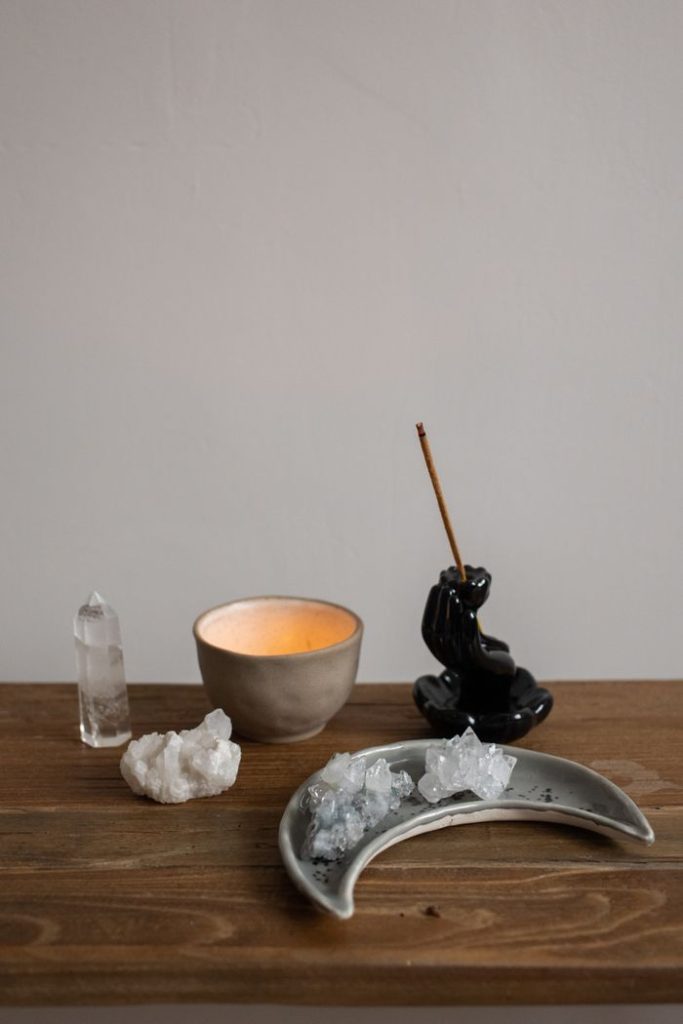 Calming setup with crystals, a lit candle, and incense on a wooden table.