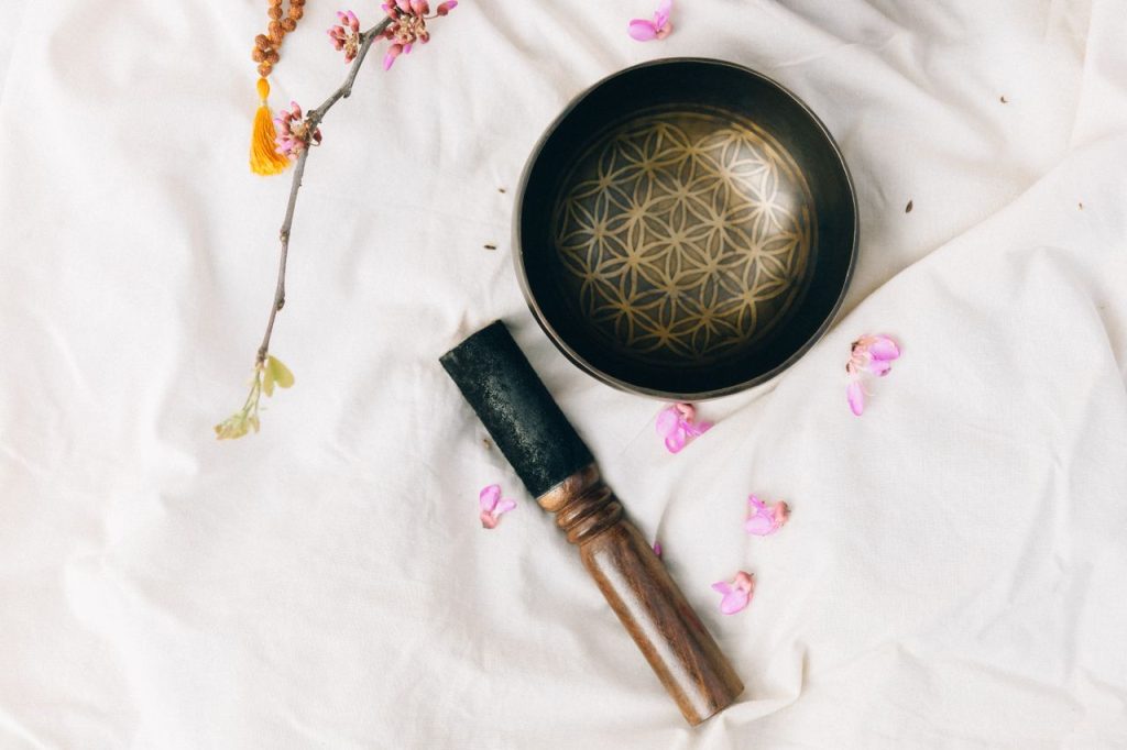 A Tibetan singing bowl on a white fabric surrounded by pink petals and branch, creating a serene atmosphere.